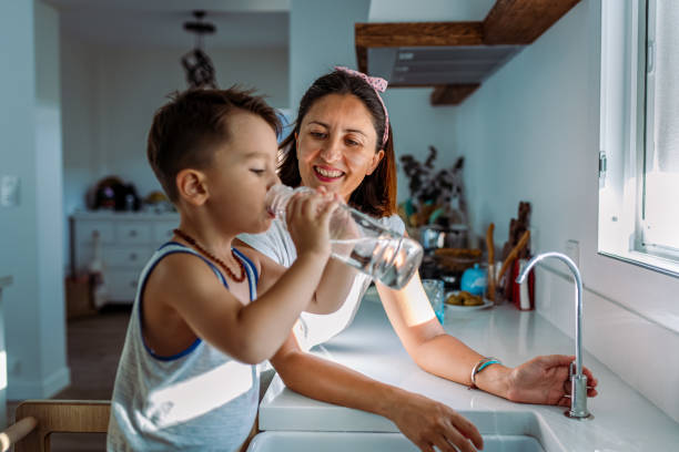 Home mother and her toddler filling a glass with filtered water right from the tap
